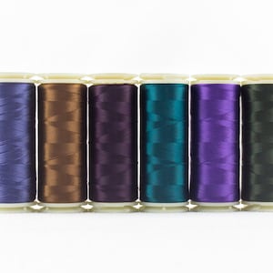 May include: A row of six spools of thread in various colors, including purple, brown, teal, and green. The thread is tightly wound on white spools, creating a visually appealing display. Ideal for sewing and crafting projects.