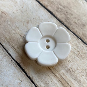 May include: White plastic flower-shaped button with two holes in the center.