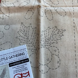 May include: A beige linen fabric with a hand-printed design of leaves and branches. The fabric is for a cross-stitch project called "Little Gathering" and is 12 inches by 12 inches. The fabric is 85% cotton and 15% linen.
