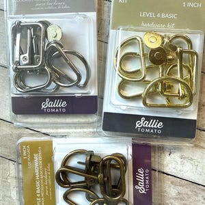 May include: Three Sallie Tomato hardware kits in silver, gold, and antique brass finishes. Each 2.54 cm kit contains metal D-rings, swivel snap hooks, and magnetic snaps in clear plastic blister packaging with branded labels and text.