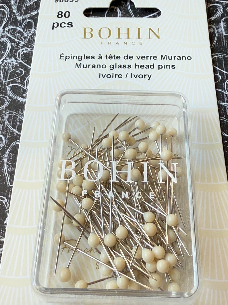 Peut inclure: Un r&eacute;cipient en plastique transparent rempli de 80 &eacute;pingles &agrave; t&ecirc;te de verre de couleur ivoire. Les &eacute;pingles sont fabriqu&eacute;es par Bohin France. Le r&eacute;cipient est &eacute;tiquet&eacute; "&Eacute;pingles &agrave; t&ecirc;te de verre Murano Murano glass head pins Ivoire / Ivory".