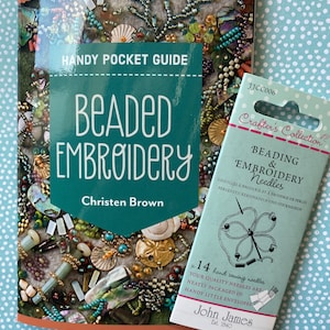 May include: A "Beaded Embroidery" book by Christen Brown, with a teal cover, next to a package of "Beading & Embroidery Needles" by John James. The book cover features a close-up of beaded embroidery. The needle package is light green.