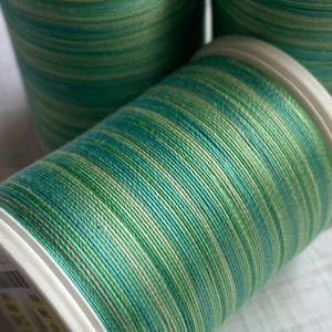 May include: Three spools of green and cream colored thread. The thread is wound around white spools with labels.