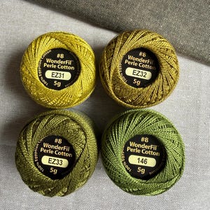 May include: Four round balls of WonderFil Perle Cotton thread in shades of green and olive. Each ball is labeled #8, 100% Egyptian Cotton, 5g, and marked with color codes EZ31, EZ32, EZ33, and 146 on the black circular center labels.