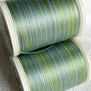May include: Two stacked spools of sewing thread featuring a variegated color pattern of light green, lime green, and soft blue vertical stripes. The spools have white plastic ends and are wound with a smooth, consistent thread texture throughout.