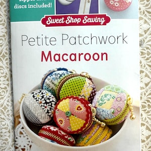 May include: A book titled "Petite Patchwork Macaroon" by Sweet Shop Sewing. The cover features a bowl of colorful fabric macaroons with zippers and a close-up of a single pink macaroon with a floral pattern.
