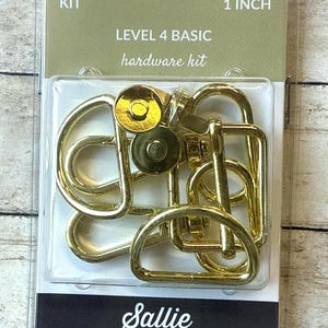 May include: A Sallie Tomato Level 4 Basic hardware kit in a clear plastic package. The kit includes gold-toned metal components such as D-rings, swivel clasps, and magnetic snaps. The packaging text reads KIT, 1 INCH, LEVEL 4 BASIC hardware kit.