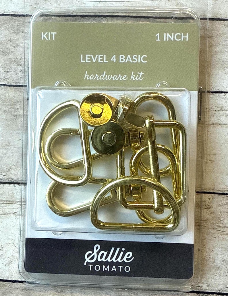May include: A Sallie Tomato Level 4 Basic hardware kit in a clear plastic package. The kit includes gold-toned metal components such as D-rings, swivel clasps, and magnetic snaps. The packaging text reads KIT, 1 INCH, LEVEL 4 BASIC hardware kit.