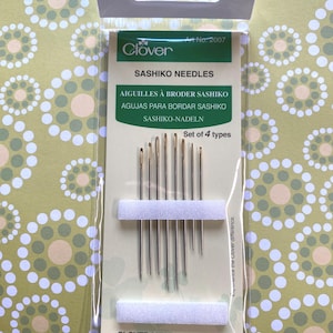 May include: A package of Clover Sashiko needles, a set of 4 types, for embroidery. The package is white with green text and a green clover logo. The needles are arranged in a row on a white foam pad.