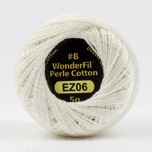 May include: A ball of off-white WonderFil Perle Cotton thread, size #8, with a black and gold label. The label indicates the thread is 5g. The thread is tightly wound, showing the texture of the cotton.