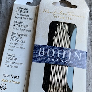 May include: A pack of 12 Bohin sewing needles, size 5/7, specifically designed for sewing thin and thick denim. The needles are made in France and are nickel plated. The packaging is blue and white with the text "Manufacture Française Depuis 1833" and "Spéciales jeans fins et épais For thin & thick jeans".