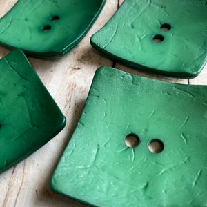 May include: Four green square buttons with a textured surface and two holes each.