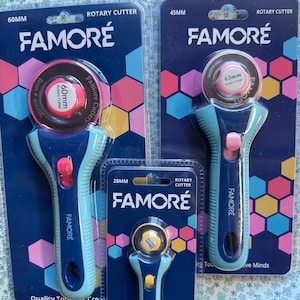 May include: Three FAMORÉ rotary cutters in blue and teal packaging. The cutters are 60mm, 45mm, and 28mm in diameter. The packaging features the FAMORÉ logo and the words "Rotary Cutter". The background has a colorful geometric pattern.