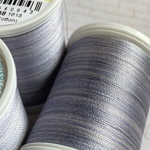 May include: Two spools of gray and silver thread. The spool on the left has a label that reads "ENDABLES col 4094 733-4094 500yds 450m 64 0 9 4 3 58 1618 Cotton)". The spool on the right has a label that reads "SULKY COTTON 30 ENDABLES 7607 4094".
