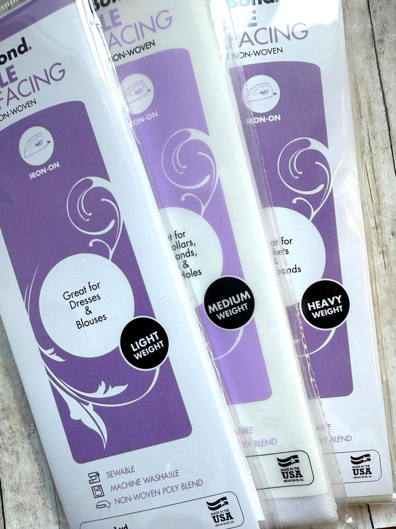 Op de afbeelding: Drie verpakkingen Pellon opstrijkbare vlieseline in lichte, medium en zware gewichten. Elke witte verpakking heeft een paarse branding met tekst waaronder Iron-On, Sewable, Machine Washable en Non-Woven Poly Blend, gemaakt in de VS.