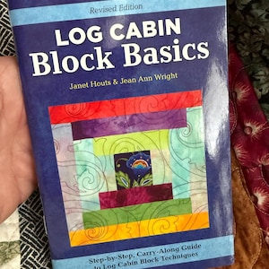 May include: A book titled "LOG CABIN Block Basics" with a colorful quilt block design on the cover. The cover features a blue background with the title in large white letters and the authors' names. The book is a step-by-step guide to log cabin block techniques.
