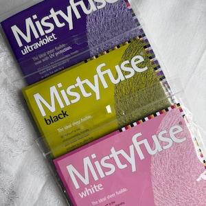 May include: Three packages of Mistyfuse, a sheer fusible web for fabric crafts. The packages are purple, yellow, and pink, with the Mistyfuse logo and product descriptions in white. The ultraviolet package has UV protection.
