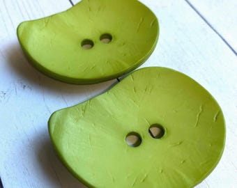 May include: Two green plastic buttons with a textured surface and two holes each.