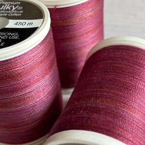 May include: Three spools of red, pink, and orange variegated thread. The spools are labeled "Premium Sulky® Blendables Apple Cotton 450 m" and "100% Cotton Use 90/12 733 7270 300406".