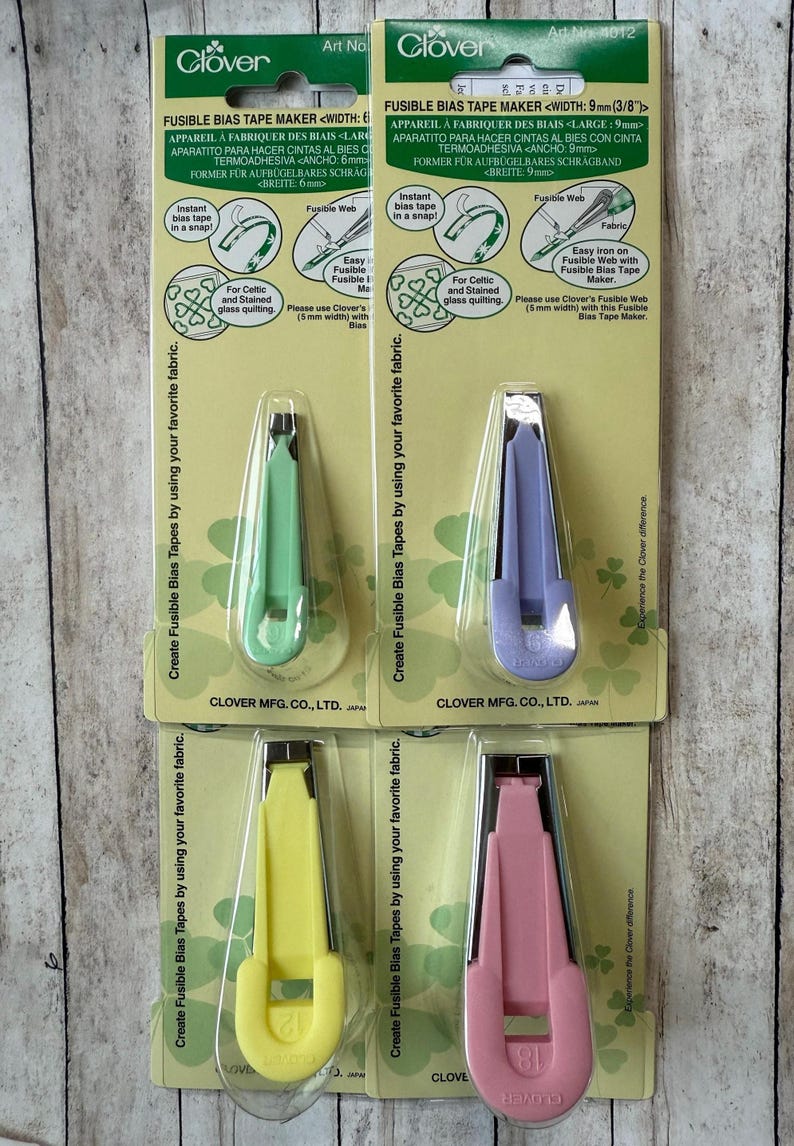 May include: Four Clover fusible bias tape makers in green, purple, yellow, and pink. Each tool is packaged on a card with instructions and the Clover logo. The tools are designed to create fusible bias tapes.