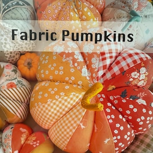 May include: A collection of fabric pumpkins in various sizes and patterns. The pumpkins are made from different fabrics, including floral, gingham, and striped designs, in shades of orange, white, and green. The text "Fabric Pumpkins" is displayed.