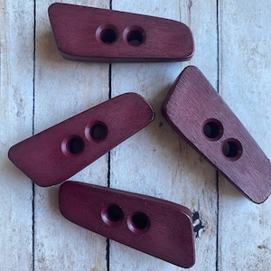 May include: Four wooden toggle buttons in a deep burgundy color. Each button has two holes for sewing.