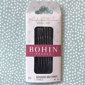May include: A package of 22 tapestry needles with a pointed tip, designed for chenille yarn. The needles are silver and come in a white and black package with the text "Manufacture Française Depuis 1833" and "BOHIN FRANCE" in red and black lettering. The package also says "Tapisserie avec pointe chenille".