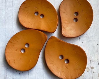 May include: Four brown, two-hole, teardrop-shaped buttons with a textured surface.