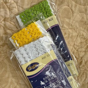 May include: Three packages of Wrights brand crochet trim in green, yellow, and white. The trim has a zigzag pattern. The packages are labeled with the numbers 400 922 and 400 030. The packaging also says "BABY PICK RACK CROCHET TURE".