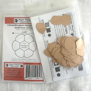 May include: Two clear plastic bags containing tan paper shapes for quilting. The left bag features a label with the text 6 Petal Miniature Hexagon, 2-3/8, and 1/2 Hexagon Center. The right bag holds a collection of small, die-cut tan paper petals.