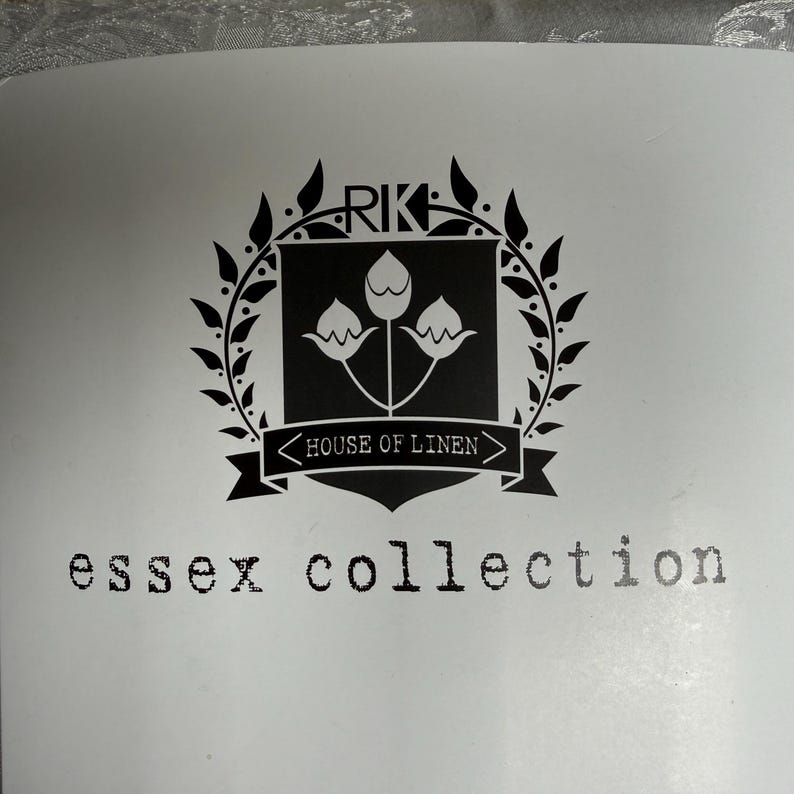 K&ouml;nnte beinhalten: Ein schwarz-wei&szlig;es grafisches Logo mit einem Wappen, das drei stilisierte Bl&uuml;tenknospen zeigt und von einem Lorbeerkranz umgeben ist. &Uuml;ber dem Wappen stehen die Buchstaben RK. Unter dem Wappen befindet sich ein Banner mit dem Text HOUSE OF LINEN und essex collection.