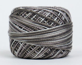 May include: A ball of variegated yarn in shades of gray, white, and lavender. The yarn is tightly wound, with visible strands creating a textured surface. Ideal for knitting or crochet projects.