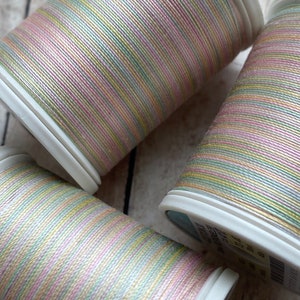 May include: Three spools of multi-colored thread with a pink, green, and yellow color scheme. The thread is wound around white plastic spools.