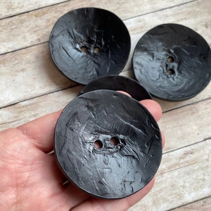 May include: Three black, round buttons with a textured surface and two holes each. The buttons are approximately 1.5 inches in diameter.
