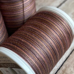 May include: Close-up of three spools of Sulky Cotton 30 thread. The thread is a blend of brown, bronze, and pink hues. The spools have white plastic sides. The text "COTTON 30" and "SULKY" are visible on the spool.