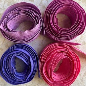 Puede incluir: Cuatro carretes de cinta de cremallera en diferentes colores: morado, rosa, azul y un rosa más oscuro. Los carretes están dispuestos en un patrón cuadrado sobre un fondo floral.