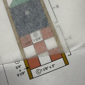 Op de afbeelding: Een naaipatroon gedrukt op papier met een doorschijnende overlay. Het patroon bevat geometrische vormen gelabeld A, B, C en D, met gedrukte afmetingen waaronder 4 inch, 1 3/8 inch, 3/4 inch bij 9 1/8 inch en 1 1/8 inch bij 3 inch.