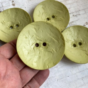 May include: Four green buttons with a textured surface. The buttons have two holes each.