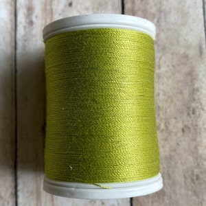 May include: A spool of bright green thread on a white plastic bobbin.