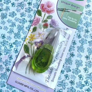 May include: A green Clover threader for embroidery needles with a clear plastic cover. The packaging features floral embroidery designs and the text "Unique design" and "Flat tip for easy threading."