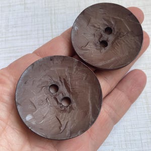 May include: Two brown, round buttons with a textured surface and two holes each.