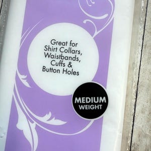 Op de afbeelding: Een verpakking van middelzware naaibare tussenvoering met een paars en wit label. De tekst op het label luidt: Great for Shirt Collars, Waistbands, Cuffs & Button Holes, en een zwarte ronde badge vermeldt: MEDIUM WEIGHT.