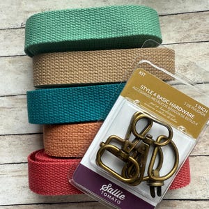 May include: A stack of five rolls of woven cotton webbing in mint green, tan, teal, peach, and coral, paired with a Sallie Tomato Style 4 Basic Hardware kit containing antique brass swivel hooks and D-rings for 1 inch wide straps.