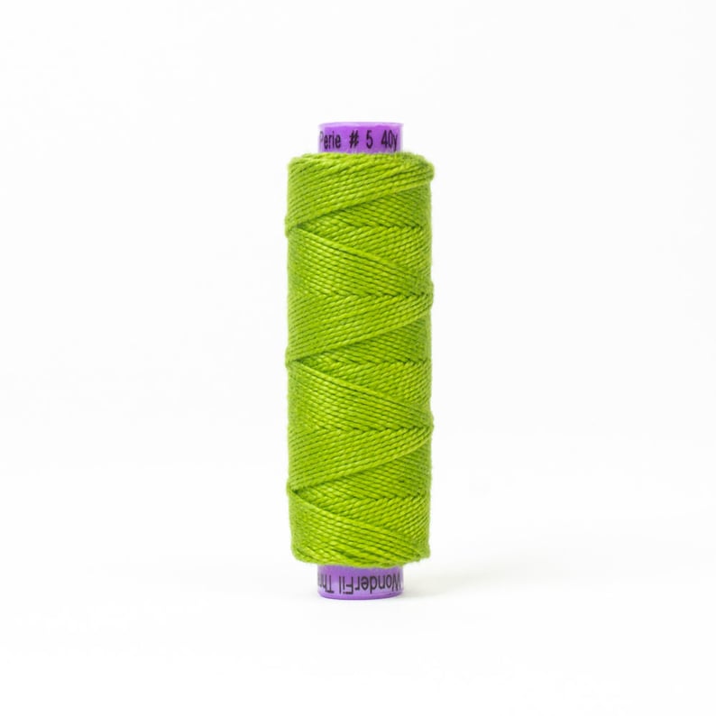 Puede incluir: Una bobina de hilo verde brillante con una etiqueta morada que dice "WonderFil 100%  Serie # 5 40y".