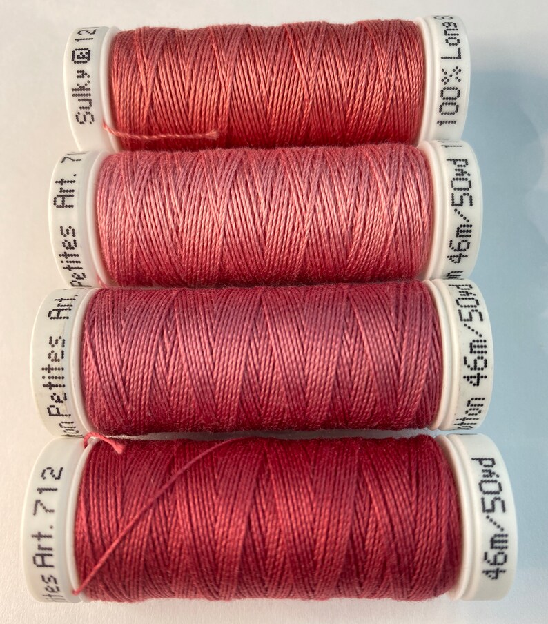 May include: Four spools of red thread, each with a white label. The labels have the text "Hes Art. 712 Petites Art. 7", "Petites Art. 7", "Sulky @ 12", and "46m/50yd 46m/50yd/ 100% Long".