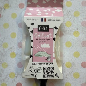 May include: A pink and white tube of OdiCoat Waterproof Gel for fabric, with a net weight of 2.12 ounces. The tube has a black cap and a white label with the product name and instructions. The label also includes a QR code and a small icon of a washing machine.