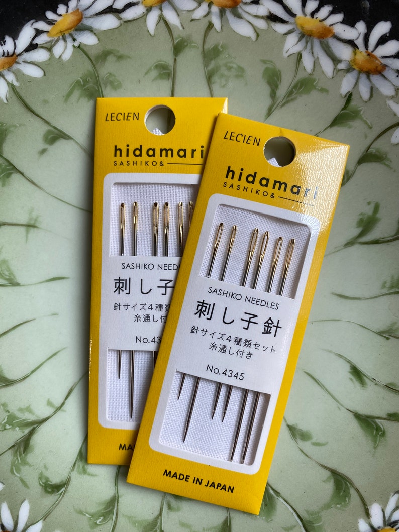 May include: Two packages of sashiko needles on a floral background. The yellow packages feature the brand name "hidamari" and Japanese text. Each package contains multiple needles, with the text "Sashiko Needles" and "Made in Japan" visible.
