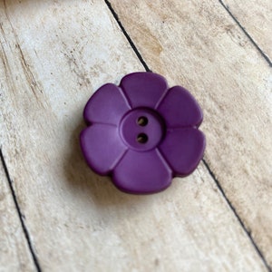 May include: A purple flower-shaped button with two holes in the center.