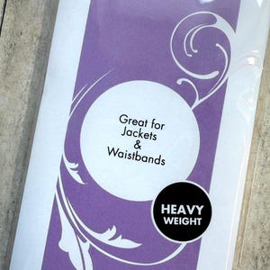 Op de afbeelding: Een rechthoekige verpakking van zware opstrijkbare tussenvoering met een paarse achtergrond en witte wervelende afbeeldingen. De tekst luidt: IRON-ON, Great for Jackets & Waistbands en HEAVY WEIGHT. De verpakking is van doorzichtig plastic.