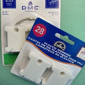 May include: A package of 28 white plastic bobbins for thread, labeled "DMC Creative World Plastic Bobbins for Thread, Cartes en Plastique pour Fils, Carreteles de Plástico".